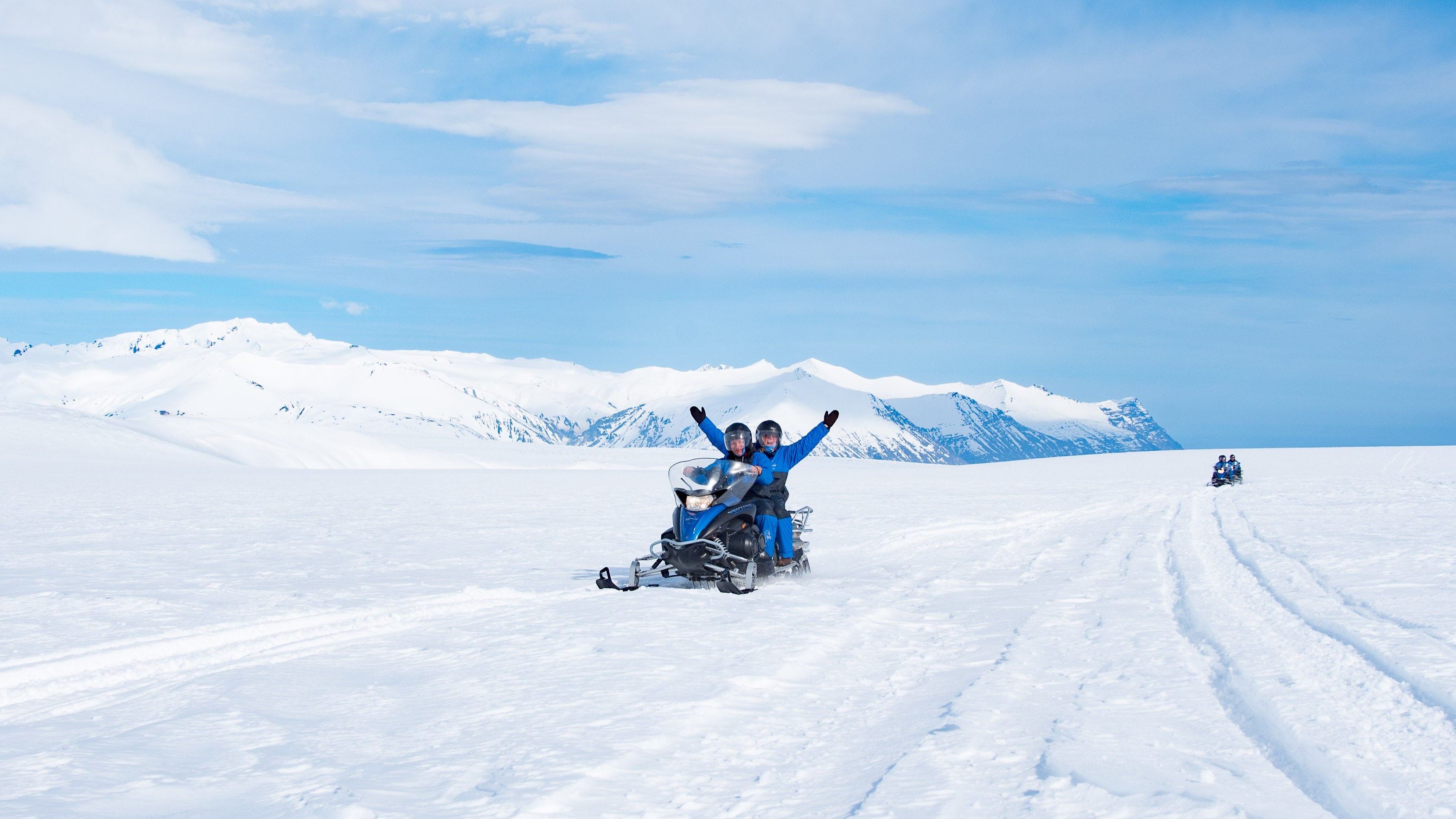To personer på snøscootertur på isbreen Vatnajokull. Passasjeren har hendene i luften.
