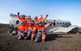 Un groupe de conducteurs de quads vêtus de combinaisons orange pose près de l'épave d'un DC-3 sur la côte sud de l'Islande.
