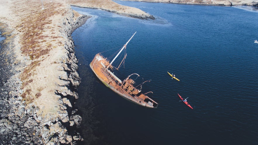 Kayakers pass a shipwreck in Iceland.