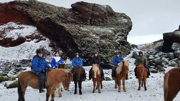 A group of riders posing for a photo in front of a geological formation in Southwest Iceland.