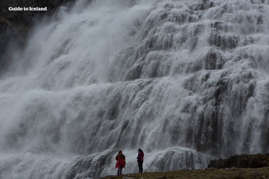 Two figures stand by Dynjandi waterfall in Iceland.