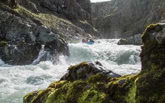 Rafting group navigating dramatic whitewater rapids in a rocky canyon surrounded by mossy cliffs in North Iceland.