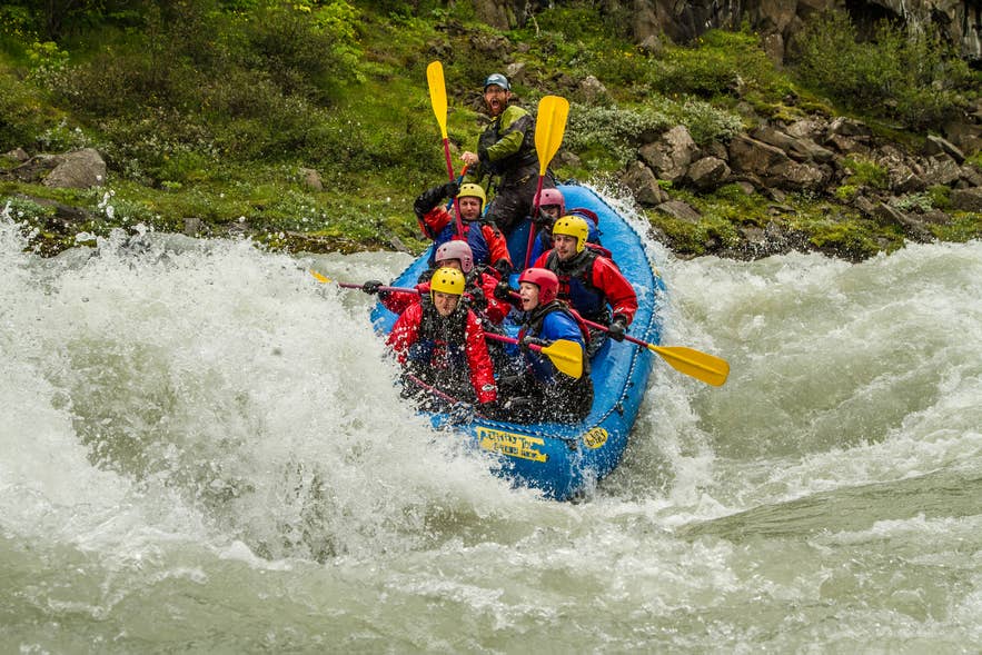 Wildwasser-Rafting auf einem Gletscherfluss im Juni in Island, mit Paddlern, die durch moosige Vulkanschluchten navigieren.