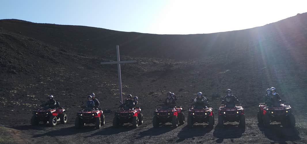 ATV riders on the Vestmannaeyjar lava fields stopped for a photo in front of a large cross.