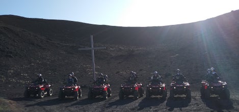 ATV riders on the Vestmannaeyjar lava fields stopped for a photo in front of a large cross.