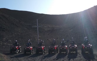 ATV riders on the Vestmannaeyjar lava fields stopped for a photo in front of a large cross.