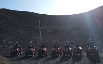 ATV-kørere på lavamarken ved Vestmannaeyjar holder pause til et foto foran et stort kors.