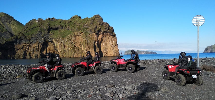 ATV riders explore Heimaey&rsquo;s black sand coast with volcanic cliffs and ocean views in South Iceland.