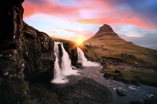 Kirkjufellsfoss-vandfaldet løber i forgrunden, mens solen går ned