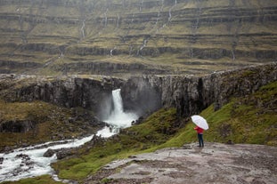 Traveler overlooking Gufufoss Waterfall in East Iceland, surrounded by dramatic cliffs and misty spray.