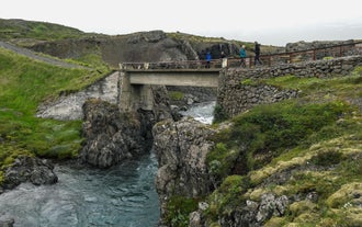 Travelers crossing a scenic bridge spanning a canyon over a river in East Iceland.