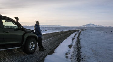 A person leans on the front of a super jeep, overlooking the snowy mountains of the Highlands.