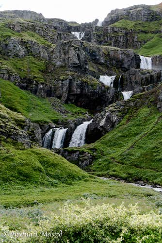 A series of cascading waterfalls tumble down a lush green hillside near Seydisfjordur, East Iceland.
