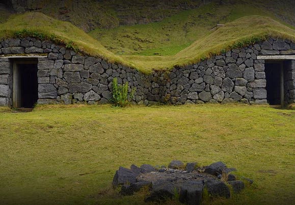 Stone-built turf houses at the old fishing station in Selatangar, Iceland, with grassy roofs and a fire pit in front.