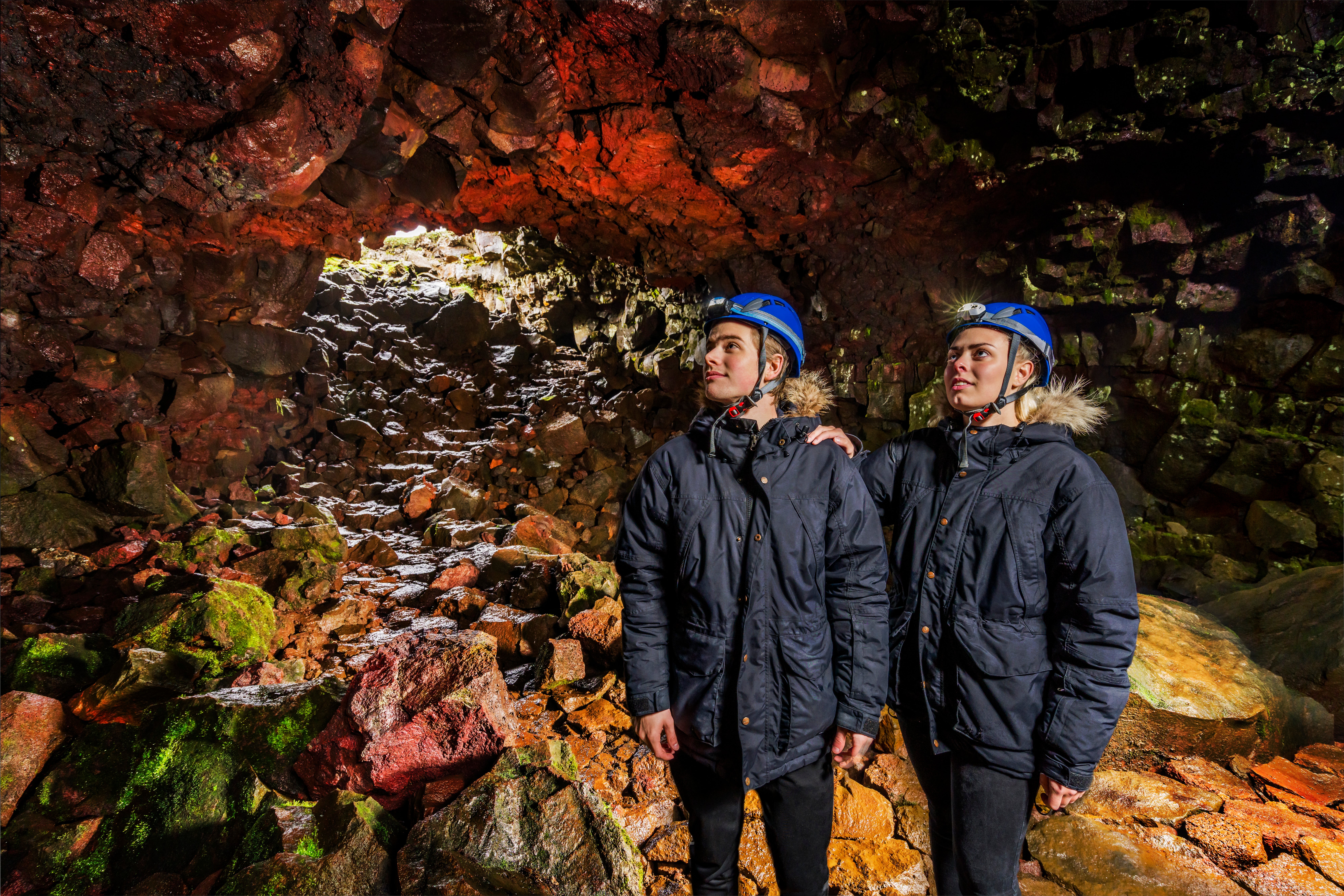 Two men wearing blue hard hats stand in the Raufarholshellir lava tunnel.