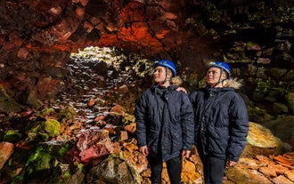 Two men wearing blue hard hats stand in the Raufarholshellir lava tunnel.