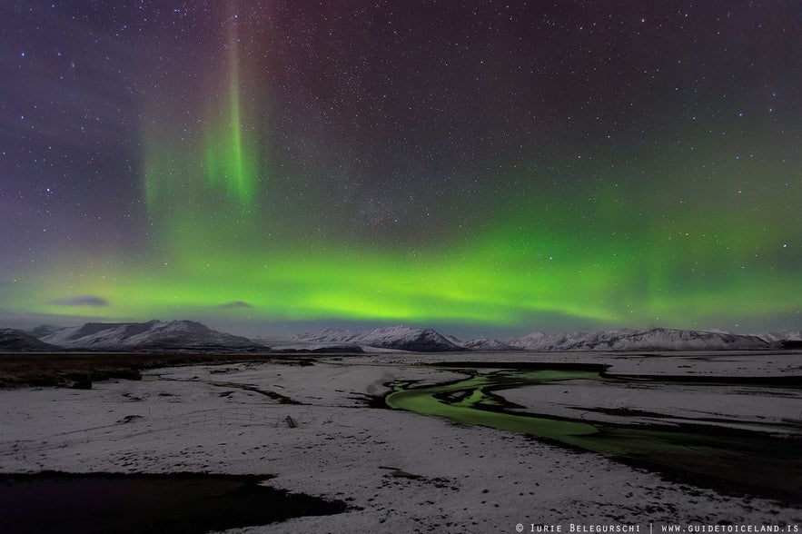 Die Nordlichter über schneebedeckten Lavafeldern und majestätischen Bergen