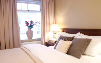 Zbliżenie wygodnego łóżka z wazonem kwiatów na parapecie w sypialni w pensjonacie BG4.