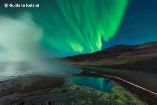 A column of steam rises before Iceland's aurora borealis.