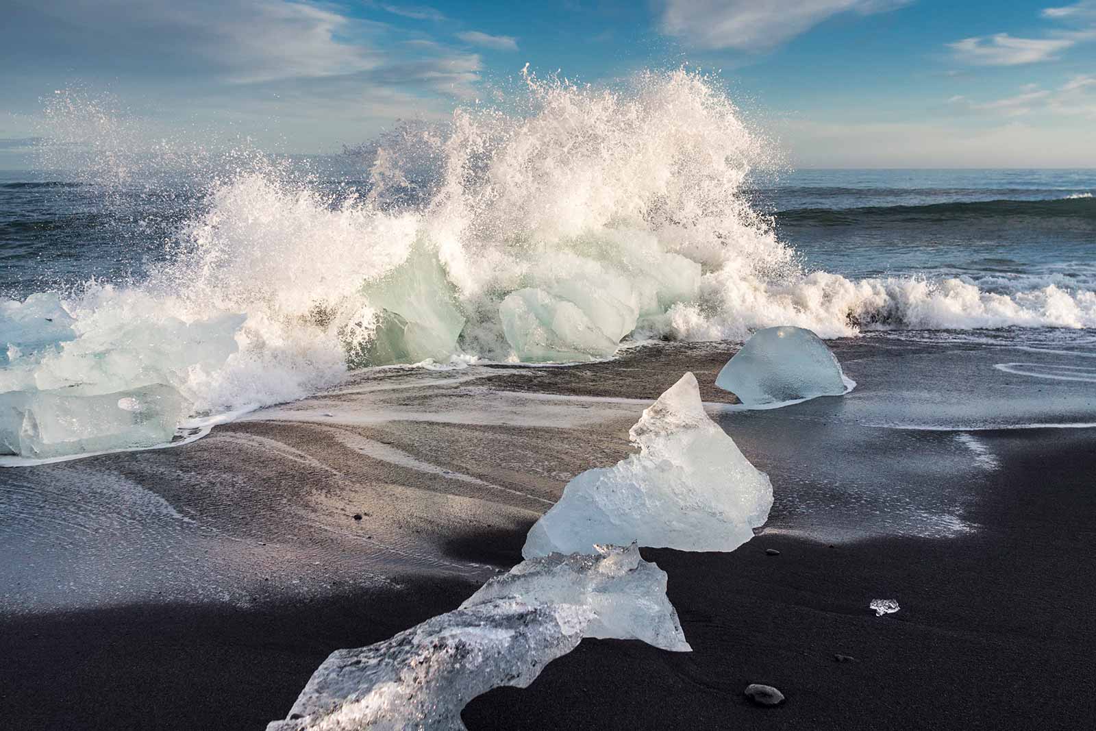 A line of icebergs washed up on Diamond Beach as a wave crashes on the shore.