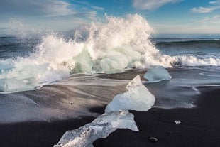 A line of icebergs washed up on Diamond Beach as a wave crashes on the shore.