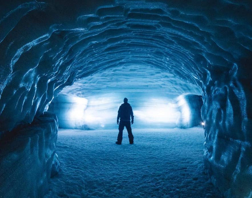 In einem leuchtenden Langjökull-Tunnel in Island steht eine Person, umgeben von geschichteten Gletscherwänden, die von innen beleuchtet werden. In einem leuchtenden Langjökull-Tunnel in Island steht eine Person, umgeben von geschichteten Gletscherwänden, die von innen beleuchtet werden.