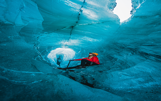 A woman on a glacier hiking tour sits on the ice.