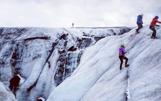 Two people scale the ice on a glacier tour on the South Coast of Iceland.