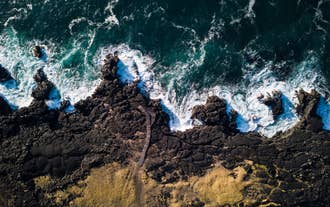 Aerial view of waves crashing against black lava cliffs on the Reykjanes coastline.