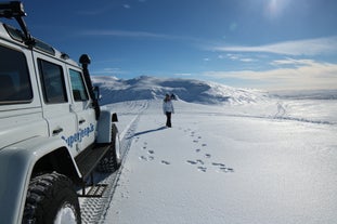 A person stands next to a super jeep on a snowy glacier in Iceland.