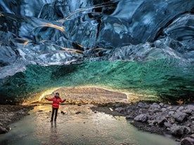 En kvinne står inne i en isgrotte med krystallblå farger.