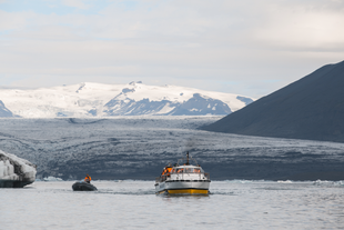 A zodiac speed boat with one person and a amphibian boat are seen sailing in the waters of the glacier lagoon in Iceland.