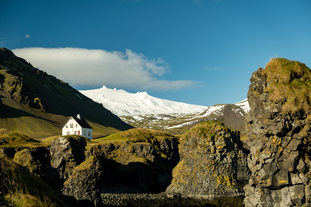 A white house is seen standing alone on top of a high hill surrounded by mountains in Arnastapi, Iceland.