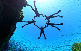 En gruppe mennesker holder hverandre i hendene i det klare vannet i Silfra-sprekken mens de snorkler.