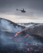 A black helicopter is flying above an active eruption in Iceland.