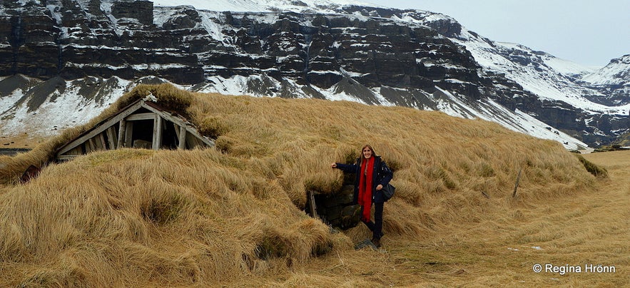 Regína by a turf outhouse by Mt. Lómagnúpur