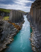 Hexagonal basalt rock column walls lining a river canyon in east Iceland.