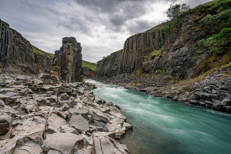 A blue tinted river flowing past a canyon of hexagonal basalt rock.