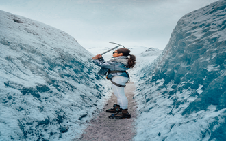 Una donna che tiene una piccozza per neve in piedi tra due pareti di ghiaccio sul ghiacciaio Sólheimajökull