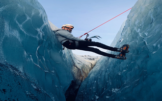 Mann beim Abstieg in eine Gletscherspalte am Solheimajökull-Gletscher mit Helm und Sicherungsseil.