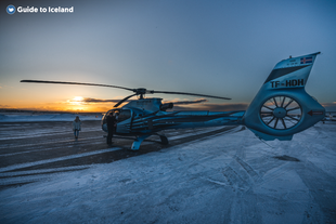 People standing near a helicopter that landed on a snowy road.