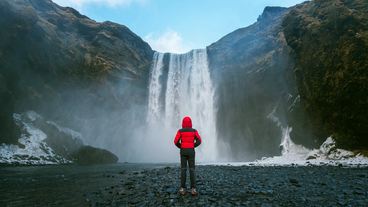 A person is standing in front of the cascading water of skogafoss waterfall.