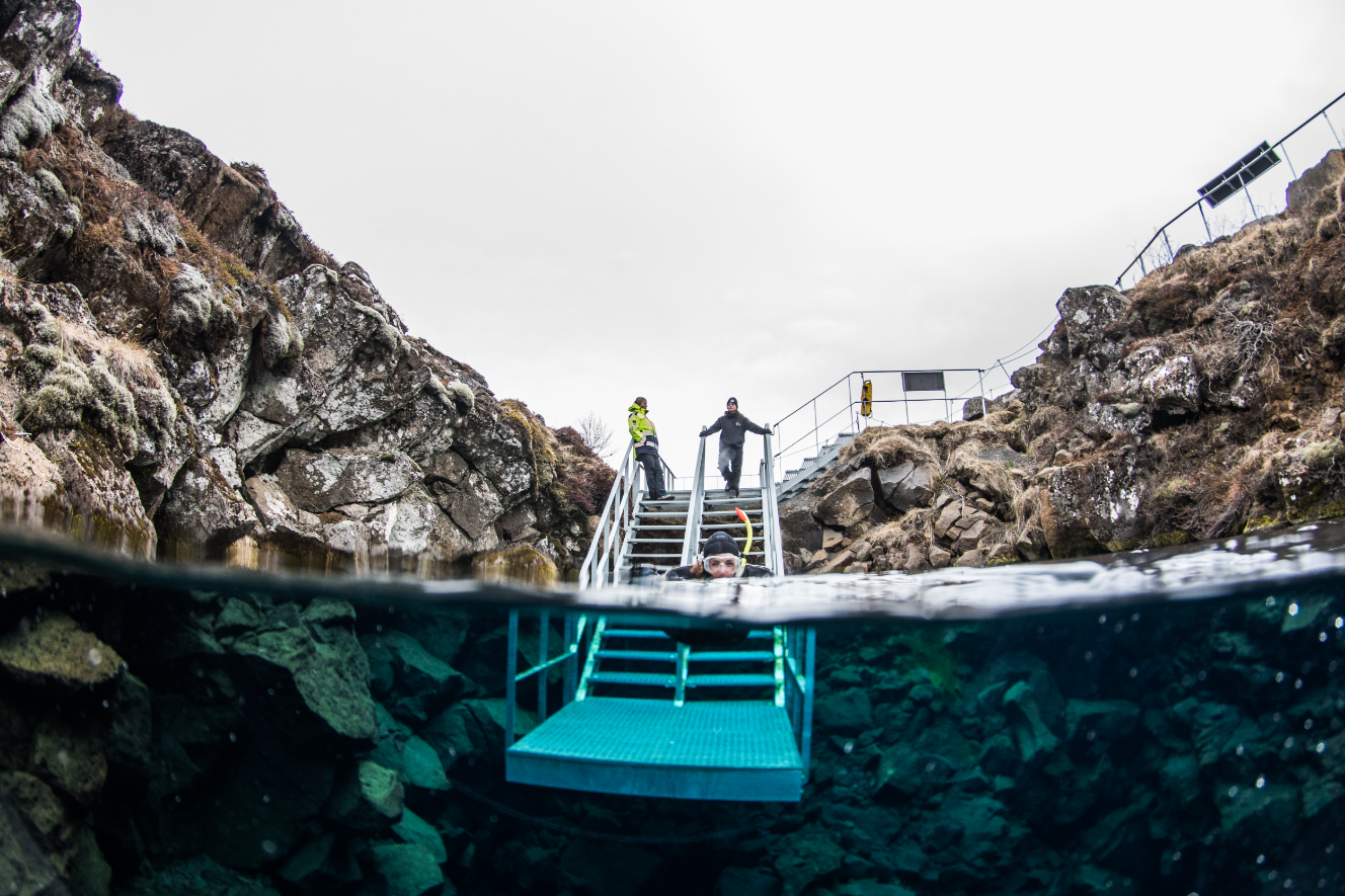 Menschen, die oben auf den Stufen stehen, welche in das klare Wasser von Silfra führen.