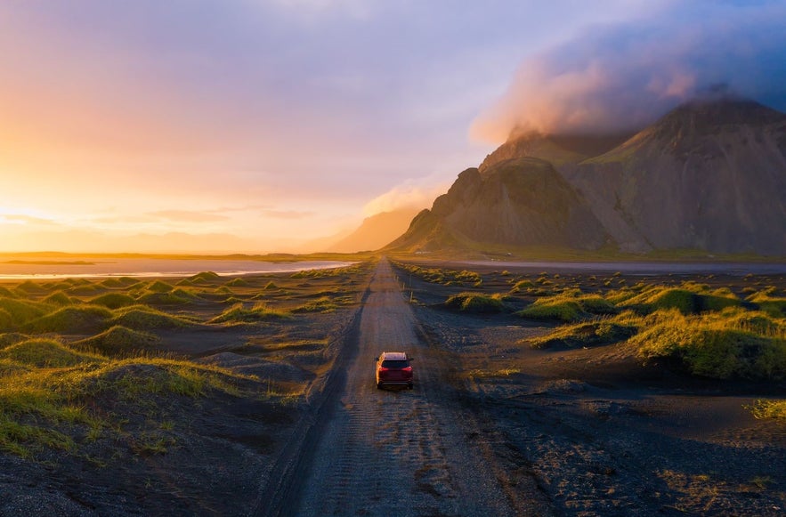 Self-drive car on an Icelandic gravel road in September, surrounded by mossy lava fields and mountains at sunset