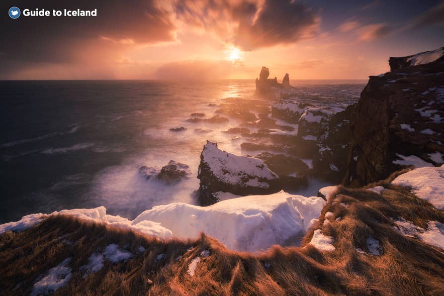 Solnedgang over de snedækkede Lóndrangar-havklipper på Islands Snæfellsnes-halvø om vinteren.