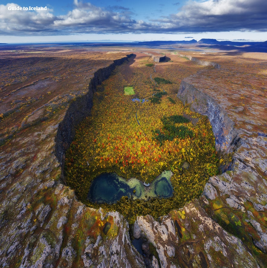 Luftfoto af Ásbyrgi-kløften i efterårsfarver med farverig skov og klipper i Vatnajökull Nationalpark. Luftfoto af Ásbyrgi-kløften i efterårsfarver med farverig skov og klipper i Vatnajökull Nationalpark.