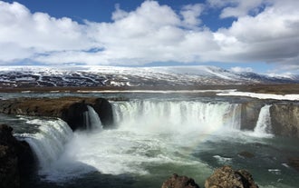 Godafoss Waterfall in spring with snowcapped mountains and a rainbow above the cascade.