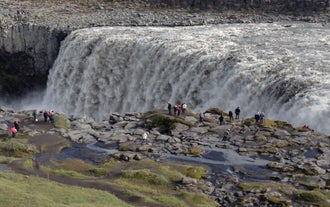 People stand near Dettifoss Waterfall in North Iceland, watching the powerful cascade drop into the canyon.