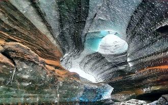 A hole is seen in the ceiling on the Katla Ice Cave with incredible black ash sand and blue ice colors.