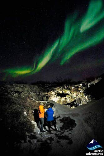 Two people watching the northern lights dance overhead.